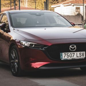 A stylish red Mazda 3 parked outdoors on a city street during sunset, showcasing urban automotive elegance.