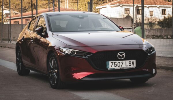A stylish red Mazda 3 parked outdoors on a city street during sunset, showcasing urban automotive elegance.