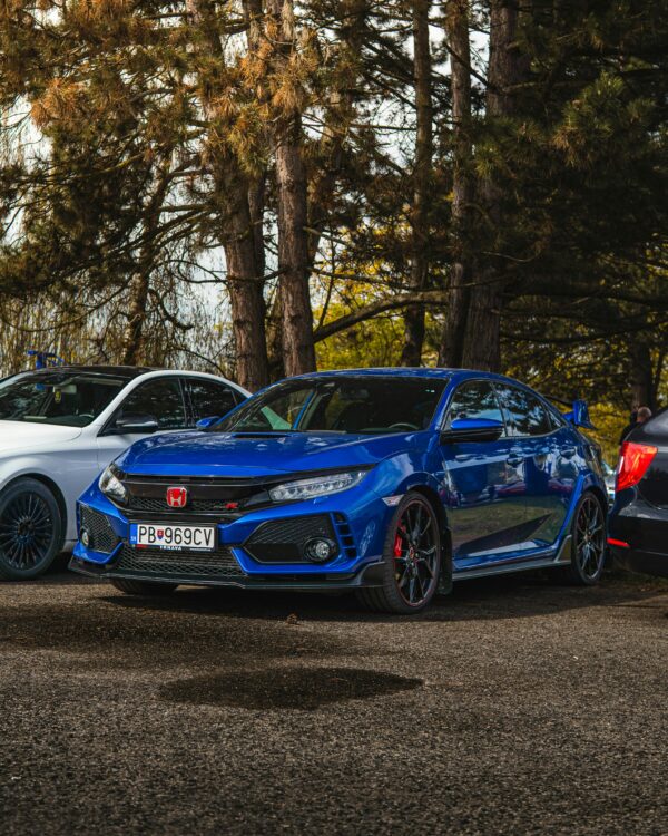A blue Honda Civic Type R is parked outdoors among trees, showcasing a sporty look.